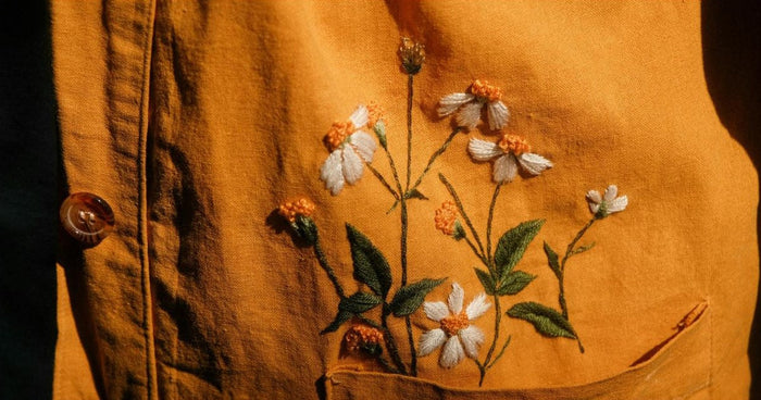 Hand embroidered white and orange daisies on the front of a mustard cotton top