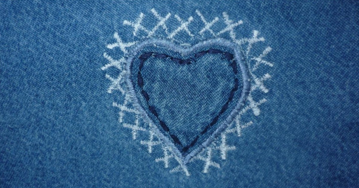 Embroidered heart with white cross stitches on blue denim jeans