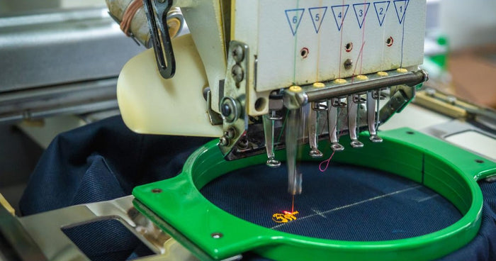 Multi-needle embroidery machine stitching a design on navy twill fabric in a green hoop