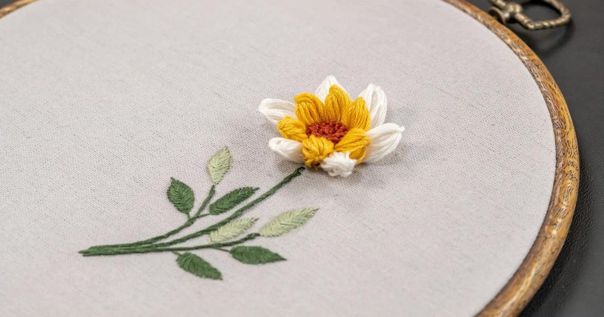 Hand embroidered flower with satin stitch leaves and padded petals on linen in a wooden hoop