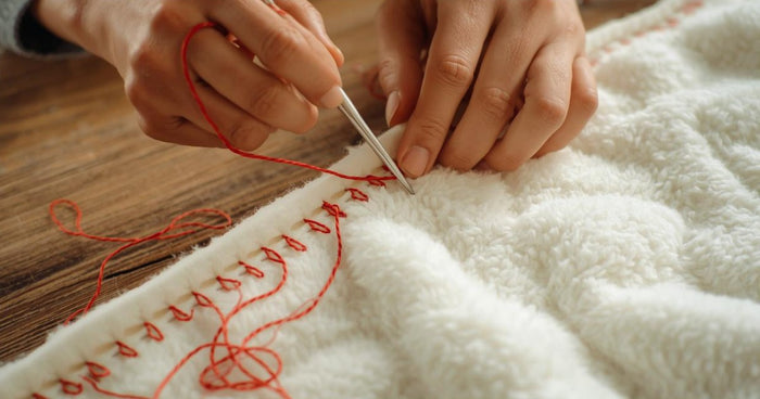 Hands sewing a red blanket stitch border along the edge of a cream fleece blanket