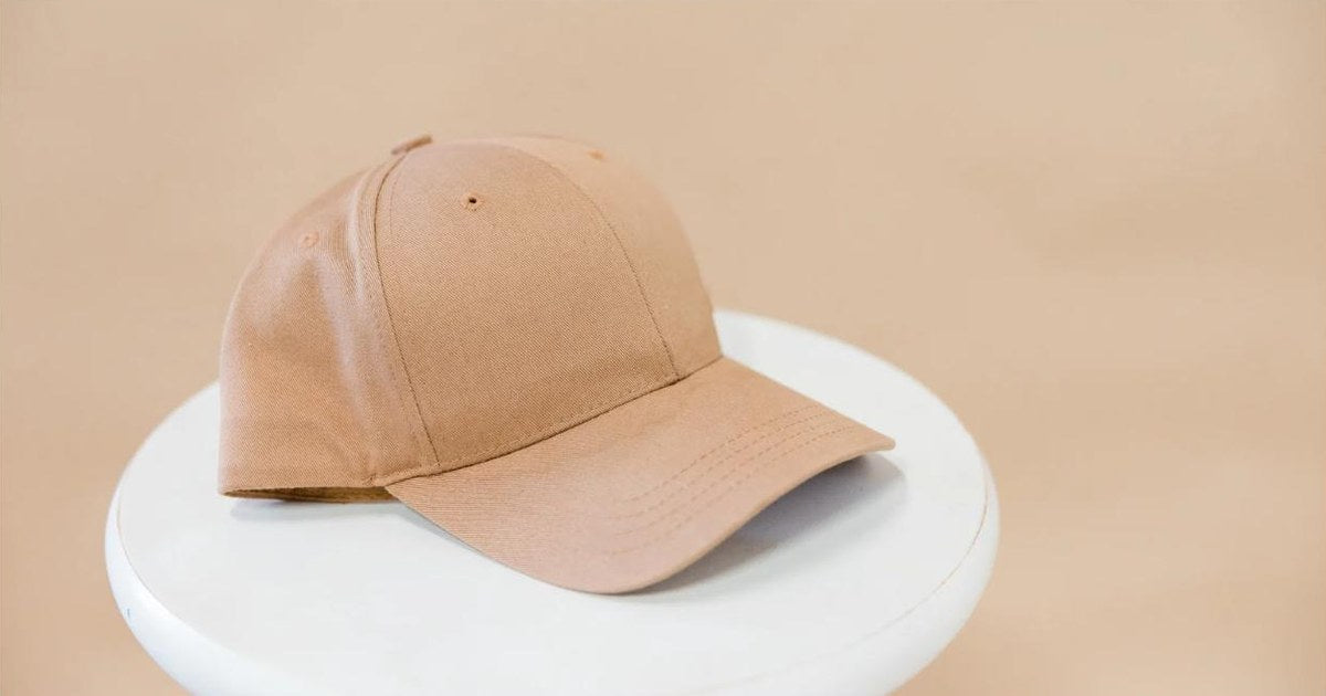 Plain tan baseball cap on a white stand, ready to be embroidered by hand