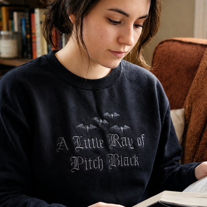 Close-up of a woman wearing an A Little Ray of Pitch Black embroidered sweatshirt with premium black on black gothic lettering and bat embroidery, perfect for fall, Halloween, and everyday wear.