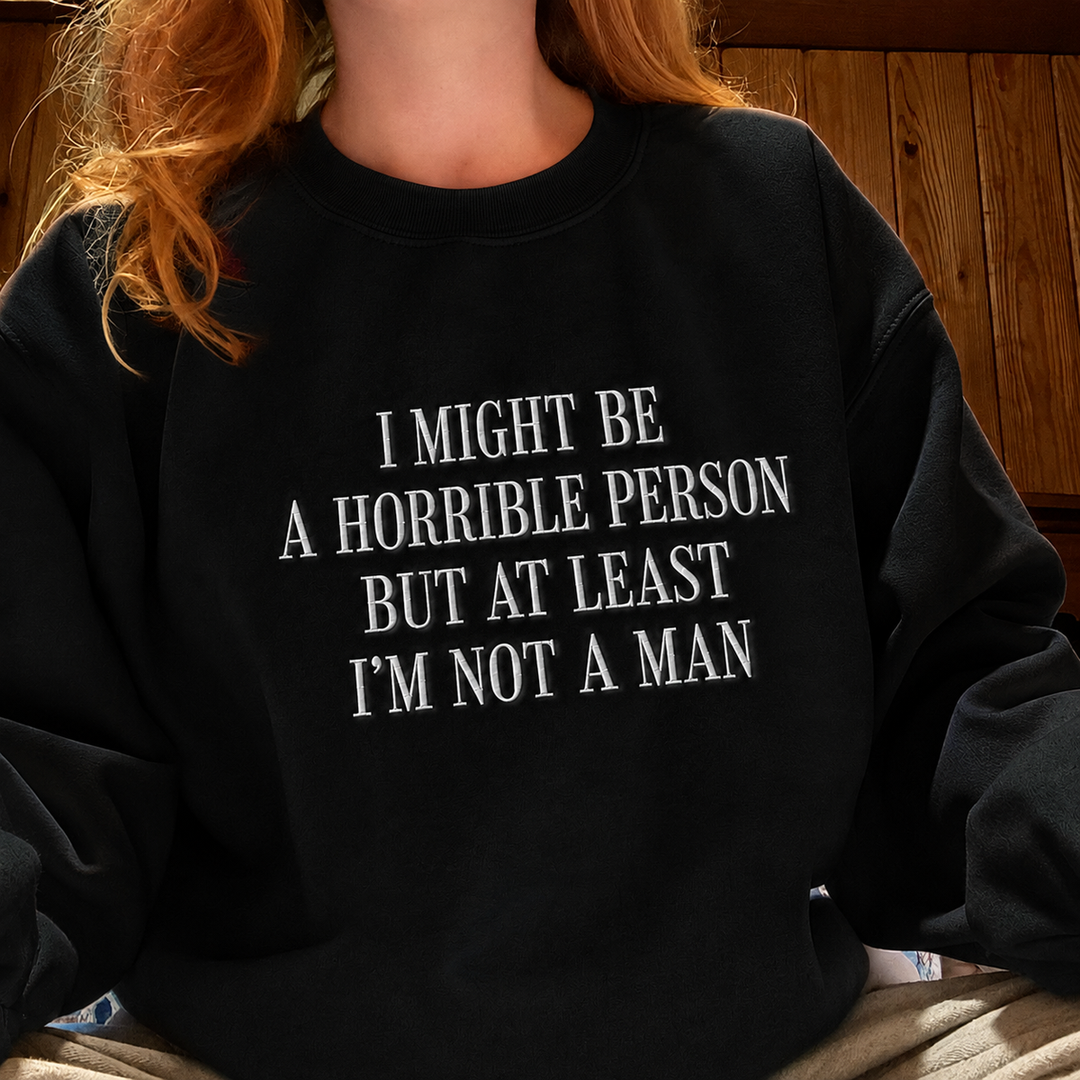 A person wearing a black crewneck sweatshirt with white text that reads 'I MIGHT BE A HORRIBLE PERSON BUT AT LEAST I'M NOT A MAN'.