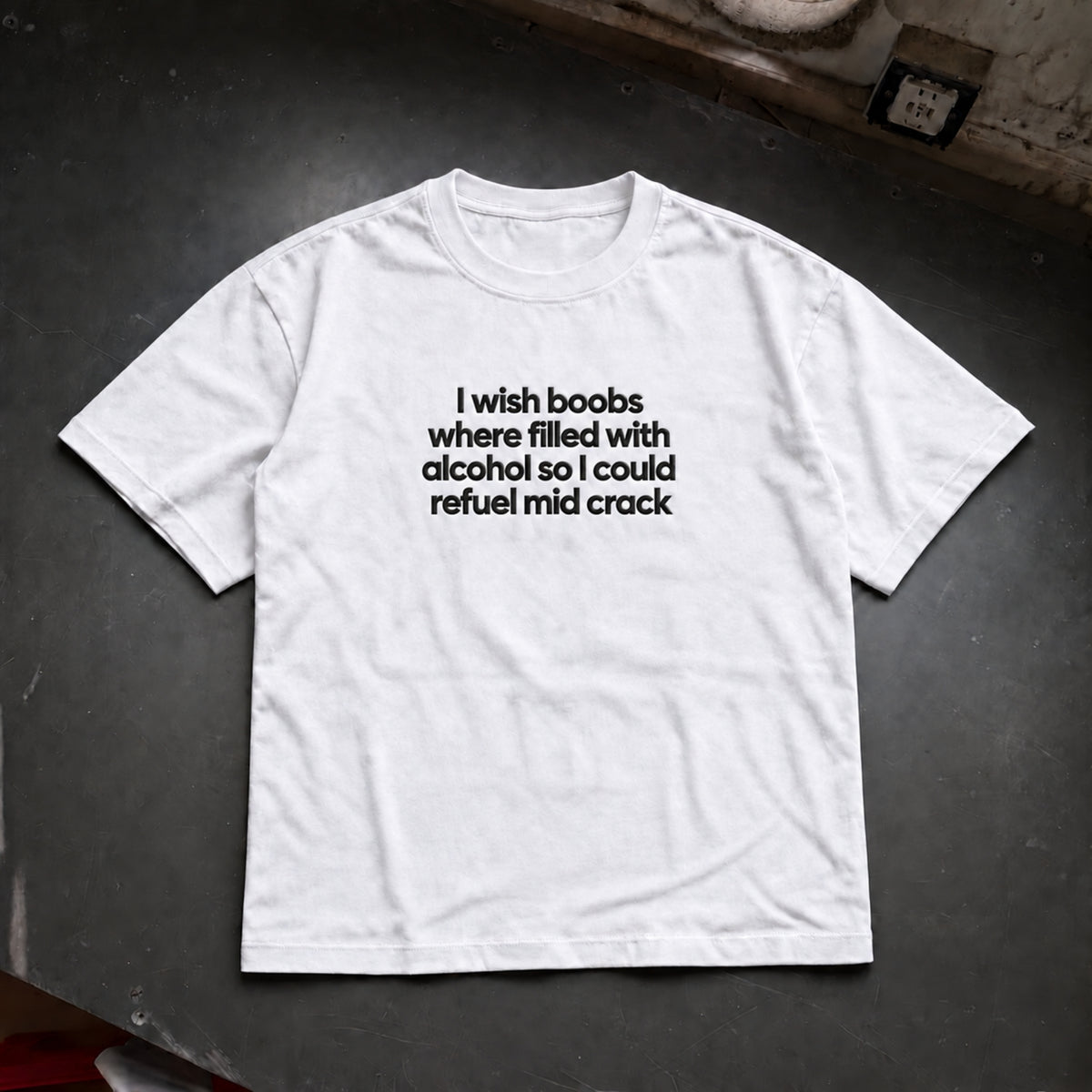 A white short-sleeve crewneck t-shirt with black printed text on the chest, laid flat on a dark gray surface.