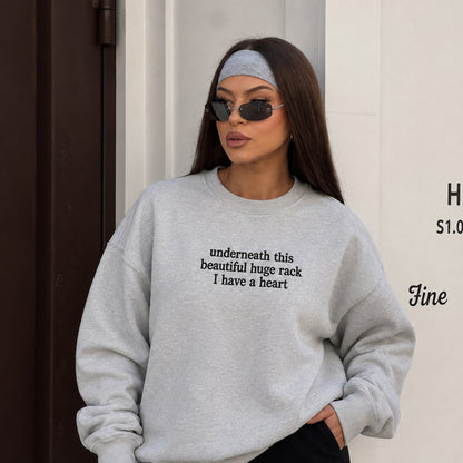 A woman wearing a light gray oversized crewneck sweatshirt with black text on the chest, styled with a gray headband and sunglasses.