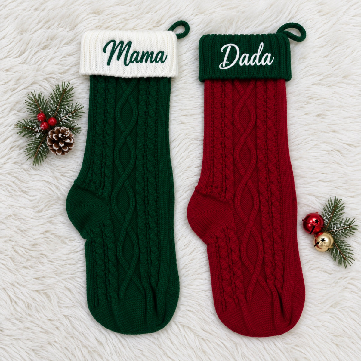 Two personalized cable-knit Christmas stockings laid flat on a white faux-fur surface. One stocking is dark green with a white cuff and the embroidered name 'Mama'; the other is red with a dark green cuff and the embroidered name 'Dada'.