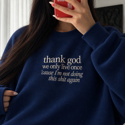 Woman wearing a navy blue embroidered sweatshirt with the white quote “thank god we only live once ’cause I’m not doing this shit again,” taking a mirror selfie indoors.
