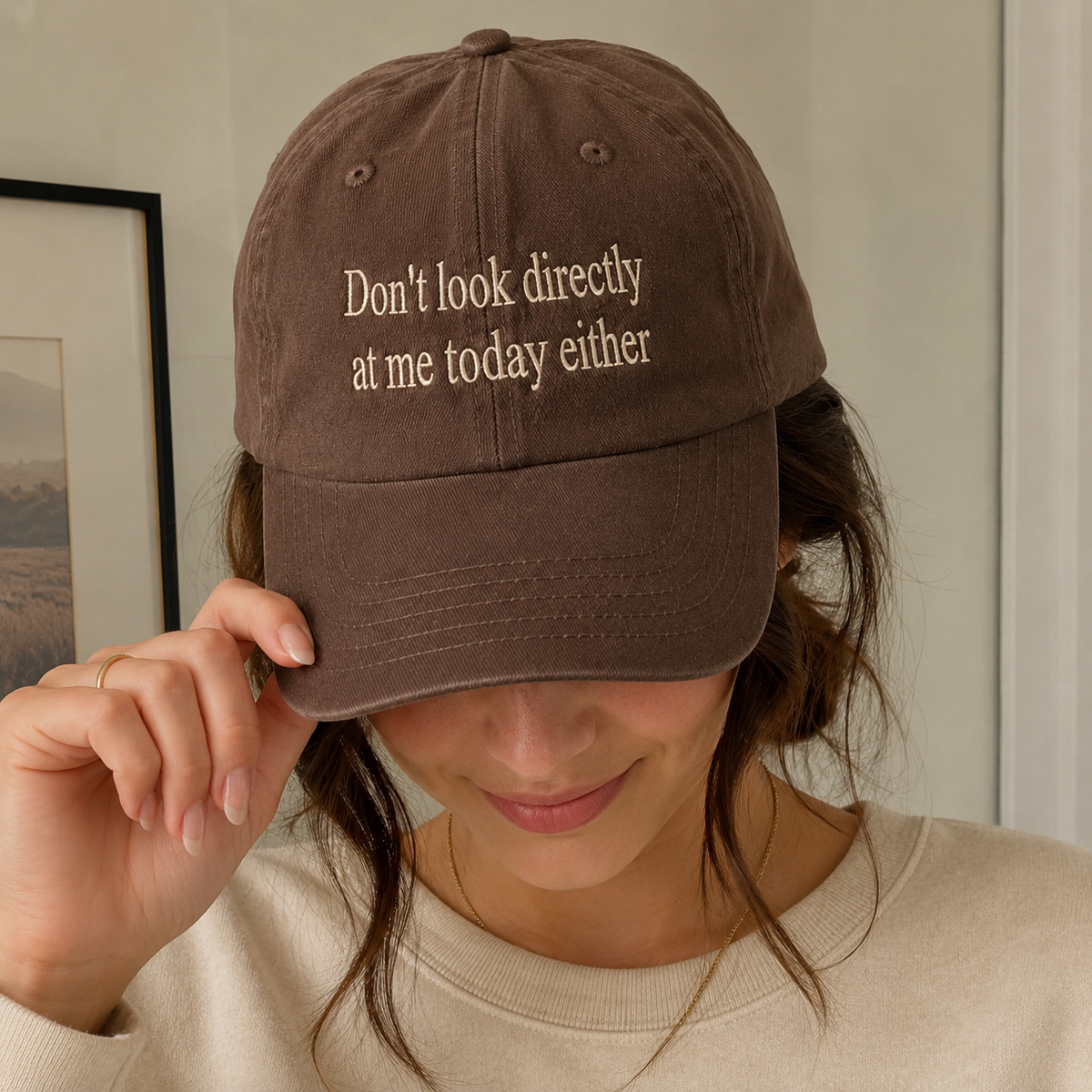 Woman wearing a brown washed baseball cap embroidered with the quote “Don’t look directly at me today either.”