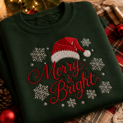 A dark forest green crewneck sweatshirt with festive Christmas embroidery featuring a red Santa hat, white snowflakes, and the words 'Merry & Bright' in red script. The sweatshirt is styled on a plaid blanket with holiday decorations like pinecones and ornaments.