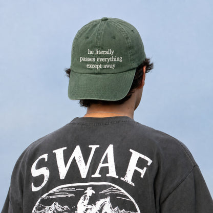 A man viewed from behind wearing an olive green baseball cap with white embroidered text and a faded black t-shirt with a large white graphic on the back. The background is a solid light blue sky.