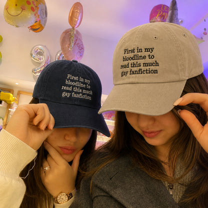 Two women wearing matching baseball caps with the text 'First in my bloodline to read this much gay fanfiction' shown in a store setting with colorful balloons in the background.