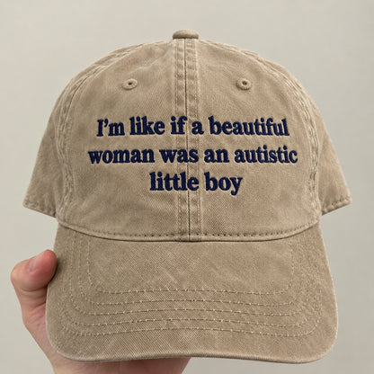 A beige cotton baseball cap held by a hand, featuring navy blue embroidered text that reads 'I'm like if a beautiful woman was an autistic little boy'.