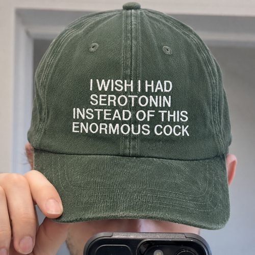 Washed dark green baseball cap with white embroidered text “I Wish I Had Serotonin Instead of This Enormous Cock,” featuring a funny dark humor mental health quote design.