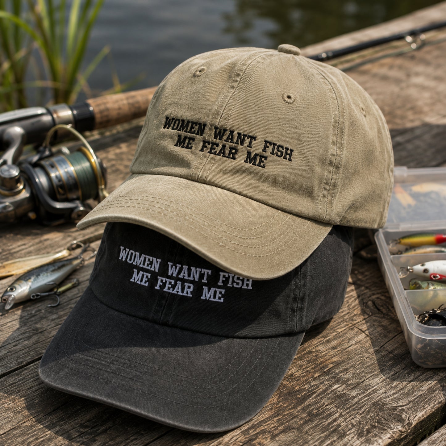 Two baseball caps with the embroidered phrase 'WOMEN WANT FISH ME FEAR ME' are displayed on a rustic wooden dock. The top cap is a warm khaki/tan color with black embroidery, and the bottom cap is black with white embroidery.