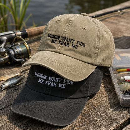 Two baseball caps with the embroidered phrase 'WOMEN WANT FISH ME FEAR ME' are displayed on a rustic wooden dock. The top cap is a warm khaki/tan color with black embroidery, and the bottom cap is black with white embroidery.