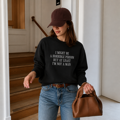 A woman wearing a black crewneck sweatshirt with white text that reads 'I MIGHT BE A HORRIBLE PERSON BUT AT LEAST I'M NOT A MAN', paired with blue jeans, a brown leather cap, and holding a brown leather handbag in an indoor hallway setting.