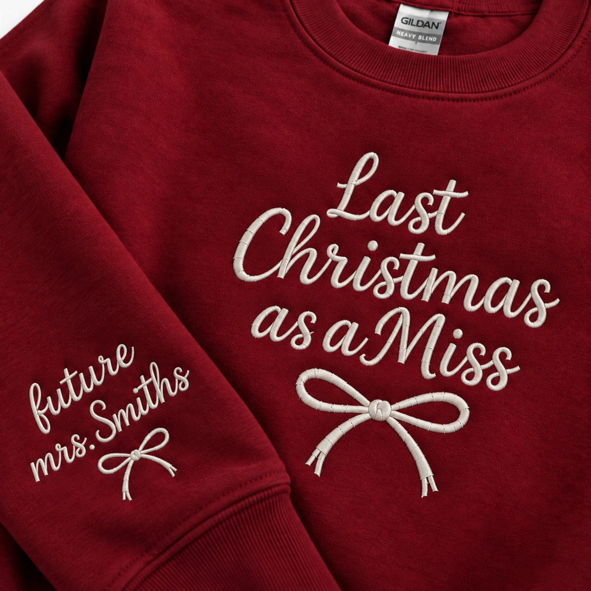 A close-up of a red crewneck sweatshirt with white embroidered text and bows. The right chest reads 'Last Christmas as a Miss' and the left sleeve reads 'future Mrs.