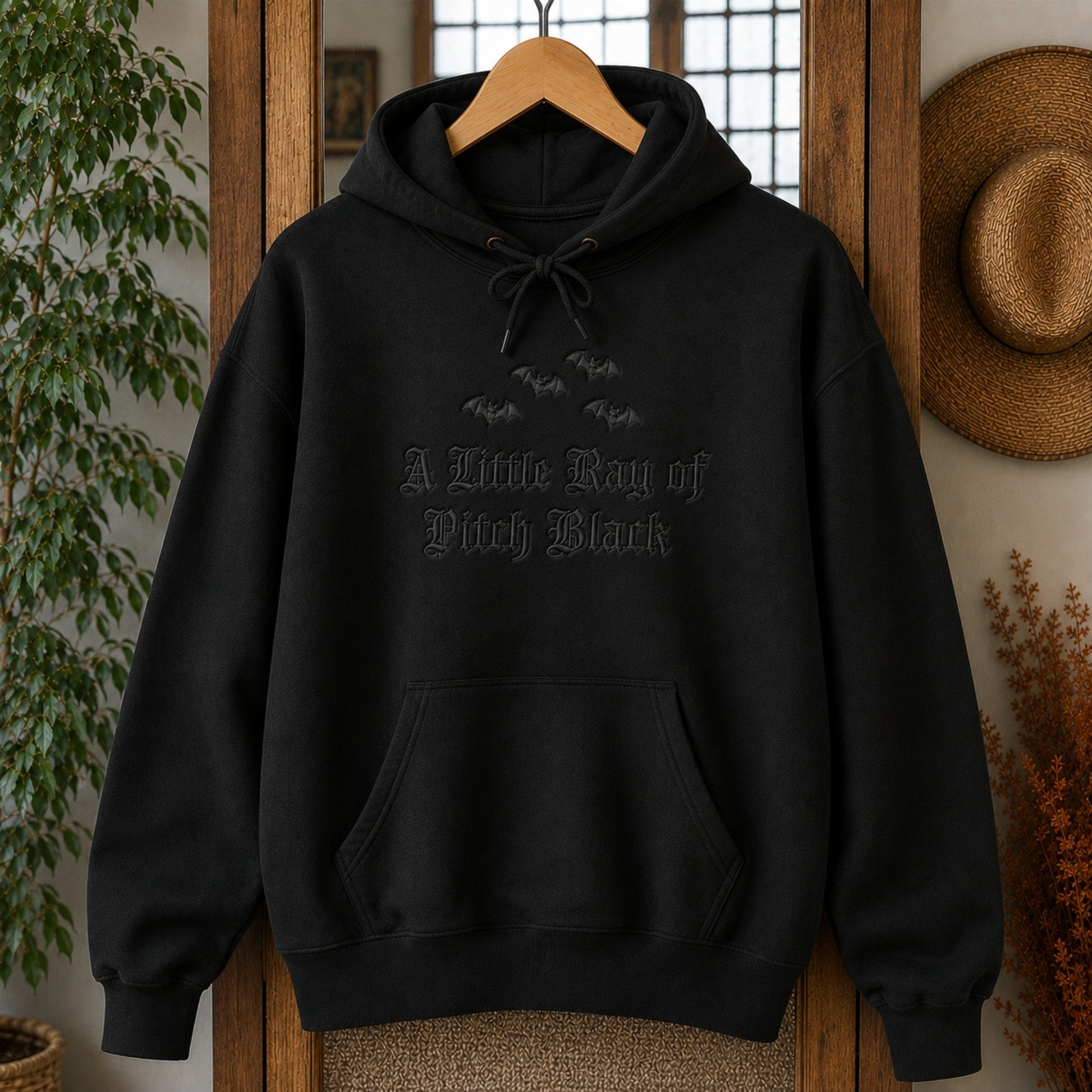 Oversized black embroidered hoodie displayed on a wooden hanger, featuring the A Little Ray of Pitch Black gothic design with premium black on black embroidery and kangaroo pocket.