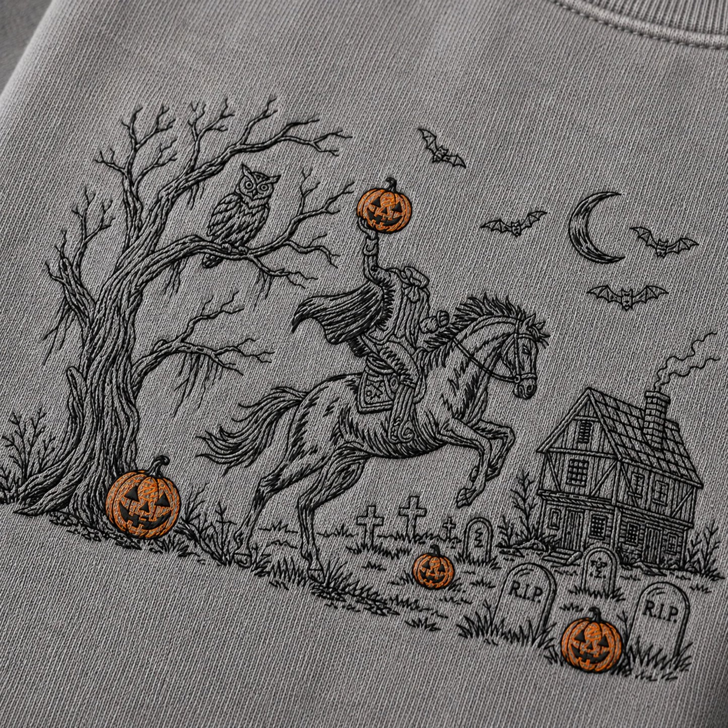 Close-up of a light gray sweatshirt featuring a detailed black line art graphic of a knight in armor on a rearing horse, holding a glowing jack-o'-lantern, with a haunted house, tombstones, bats, moon, owl, and additional pumpkins in a Halloween scene.