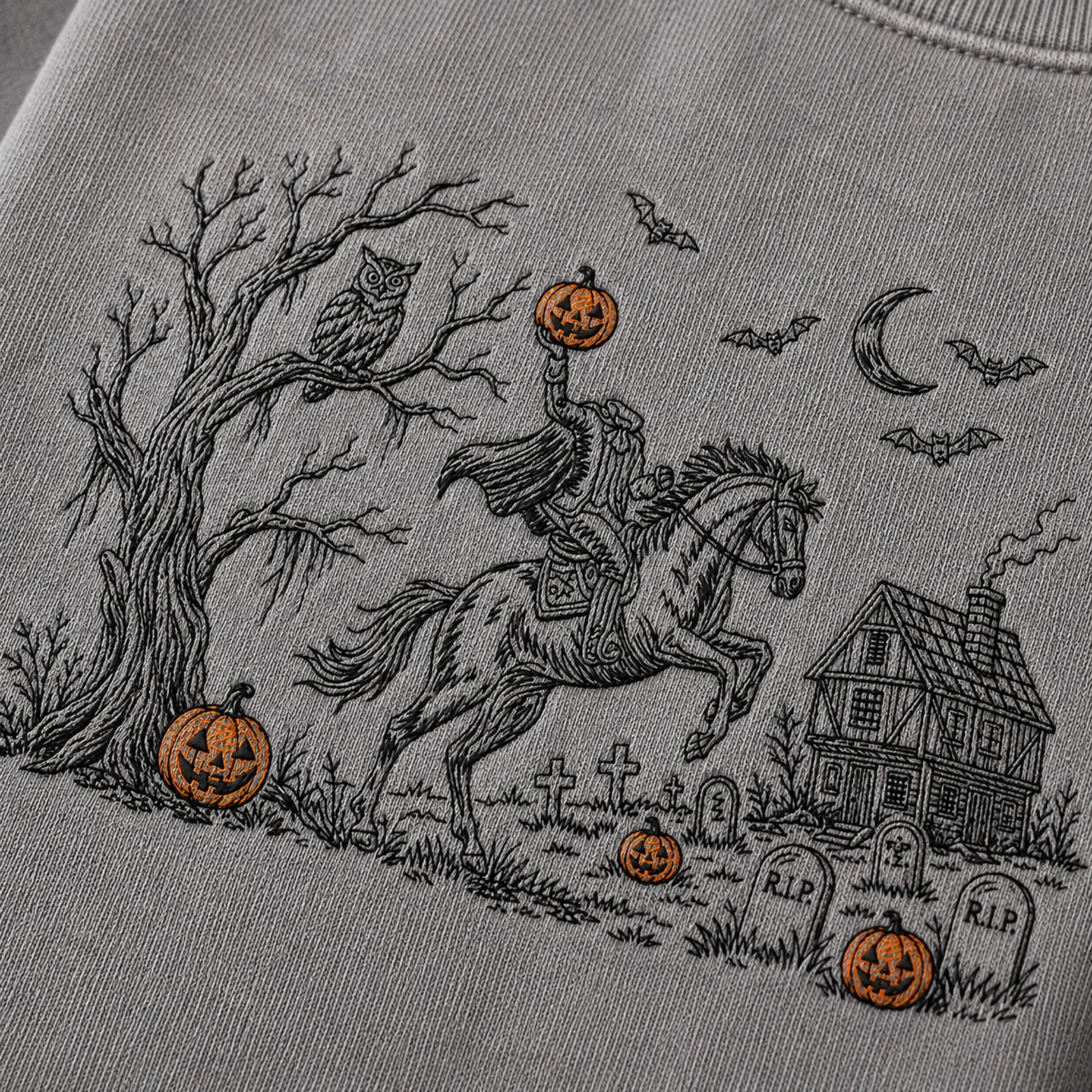Close-up of a light gray sweatshirt featuring a detailed black line art graphic of a knight in armor on a rearing horse, holding a glowing jack-o'-lantern, with a haunted house, tombstones, bats, moon, owl, and additional pumpkins in a Halloween scene.