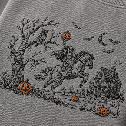 Close-up of a light gray sweatshirt featuring a detailed black line art graphic of a knight in armor on a rearing horse, holding a glowing jack-o'-lantern, with a haunted house, tombstones, bats, moon, owl, and additional pumpkins in a Halloween scene.