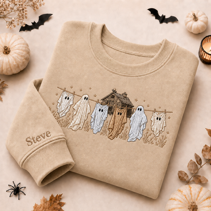 Sand beige embroidered Halloween sweatshirt featuring whimsical ghosts hanging on a clothesline with a haunted house and personalized custom name 'Steve' on the sleeve cuff.