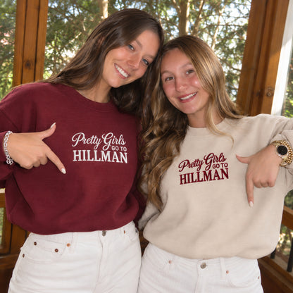 Two women posing together on a porch, each wearing a sweatshirt with the text 'Pretty Girls GO TO HILLMAN' printed on the chest. The woman on the left wears a burgundy sweatshirt, and the woman on the right wears a light beige sweatshirt.