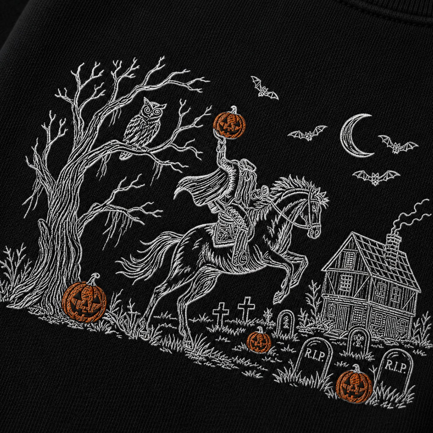 Black fabric with a white embroidered Halloween scene featuring a rider on a horse, bare tree, owl, bats, crescent moon, haunted house, tombstones, and orange jack-o'-lanterns.