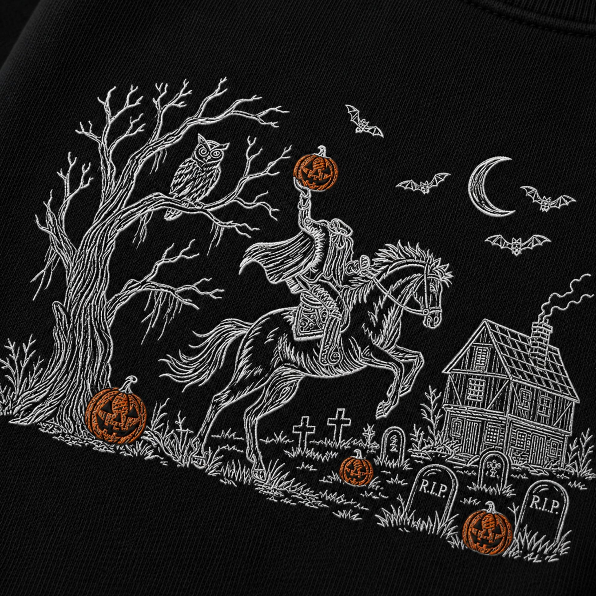 Black fabric with a white embroidered Halloween scene featuring a rider on a horse, bare tree, owl, bats, crescent moon, haunted house, tombstones, and orange jack-o'-lanterns.