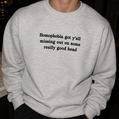 A person wearing a light heather gray crewneck sweatshirt with the text 'Homophobia got y'all missing out on some really good head' printed in black across the chest.
