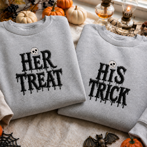 Two folded light gray crewneck sweatshirts displayed on a cozy autumn surface. One reads "HER TREAT" with a small skull above the text, and the other reads "HIS TRICK" with the same skull motif.