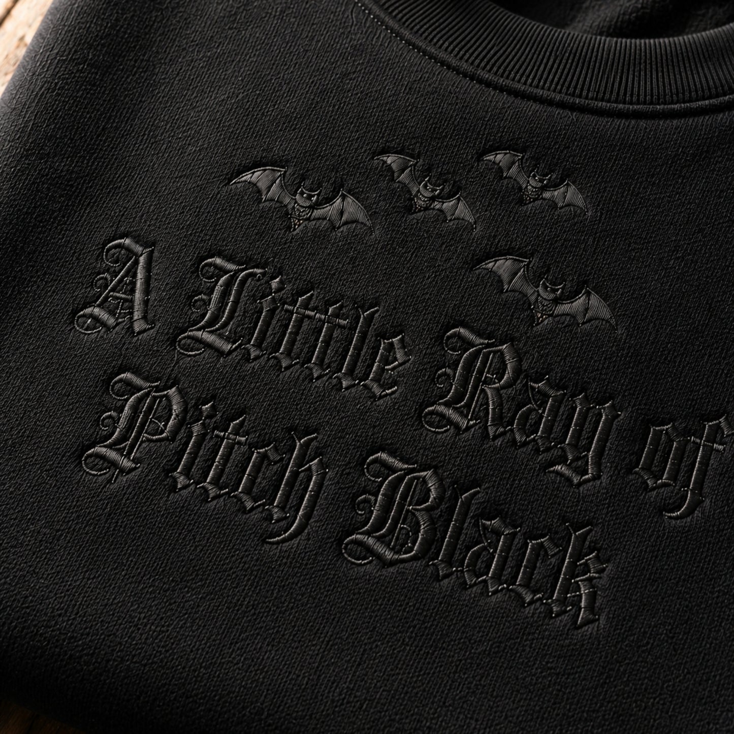A zoom-in detail of a little ray of pitch black embroidery on the black sweatshirt.