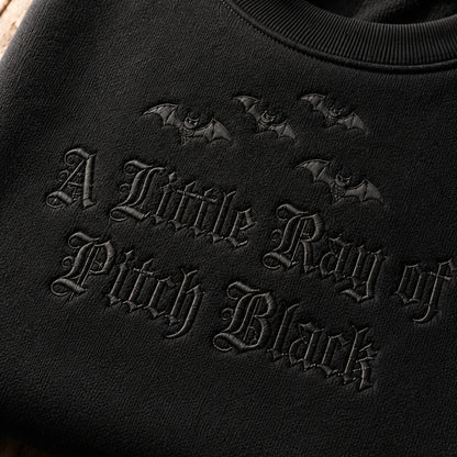 A zoom-in detail of a little ray of pitch black embroidery on the black sweatshirt.