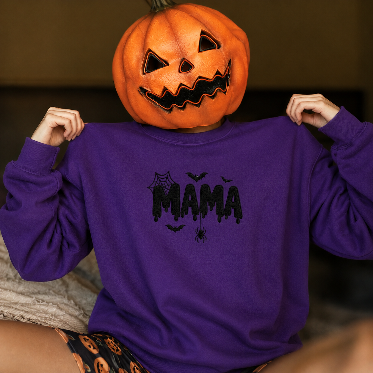 Spooky purple MAMA Halloween sweatshirt worn with a jack-o'-lantern pumpkin head mask for Halloween photoshoot.