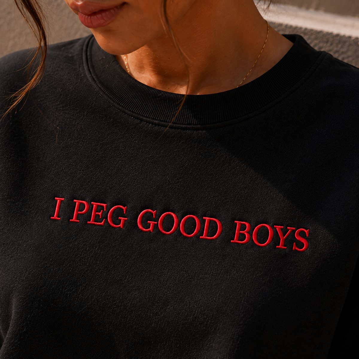 A close-up of a person wearing a black crewneck sweatshirt with the phrase 'I PEG GOOD BOYS' embroidered in red across the chest.