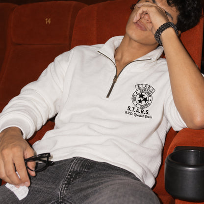 Man wearing a white quarter-zip sweatshirt with black embroidered S.T.A.R.S. Raccoon Police Department chest emblem, relaxing in a red movie theater seat.