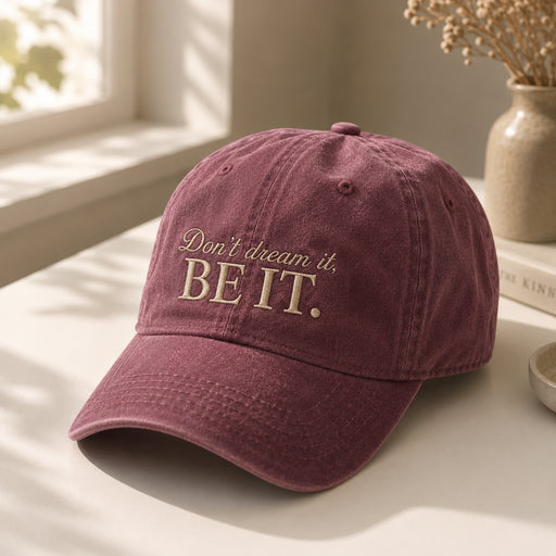 A dusty burgundy baseball cap with the embroidered text 'Don't dream it. BE IT.