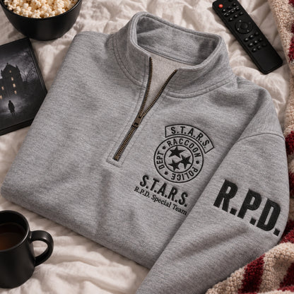 Gray quarter-zip sweatshirt with black embroidered S.T.A.R.S. Raccoon Police Department chest emblem and R.P.D. sleeve lettering, styled on a cozy bed with popcorn, coffee, a remote, and movie-night decor.