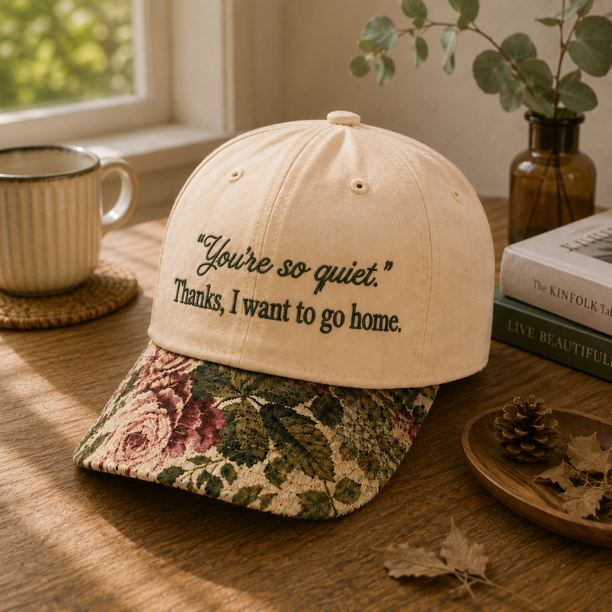 Beige embroidered baseball cap with text reading 'You're so quiet. Thanks, I want to go home.' and a brown floral rose tapestry visor.