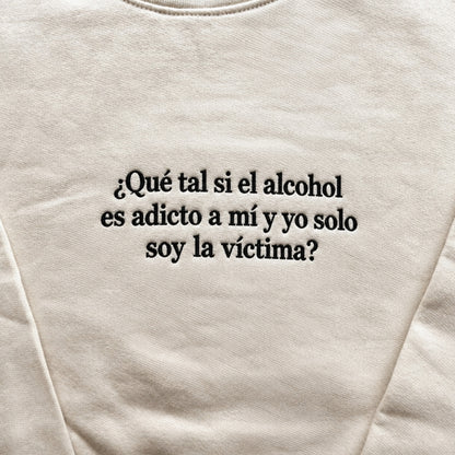 Cream sweatshirt with black embroidered Spanish quote “¿Qué tal si el alcohol es adicto a mí y yo solo soy la víctima?” centered on the chest in a bold serif font.
