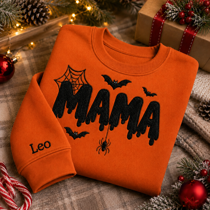 Burnt orange crewneck Halloween sweatshirt featuring black embroidered MAMA text with spiderweb, spider, and bat details, plus personalized name Leo embroidered on the sleeve.