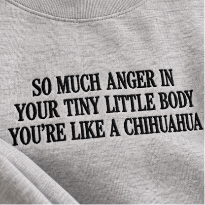 Close-up of a light gray heather crewneck sweatshirt with black embroidered text that reads 'SO MUCH ANGER IN YOUR TINY LITTLE BODY YOU'RE LIKE A CHIHUAHUA'.