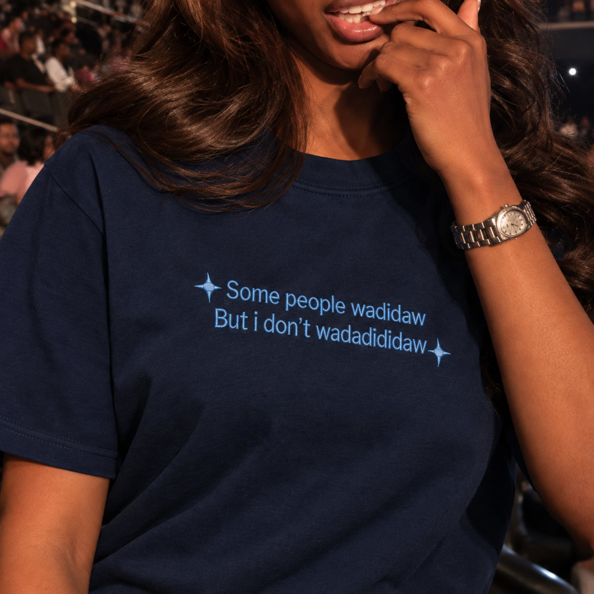 A close-up of a woman wearing a navy blue t-shirt with light blue text that reads 'Some people wadidaw But i don't wadadididaw' flanked by small star graphics.